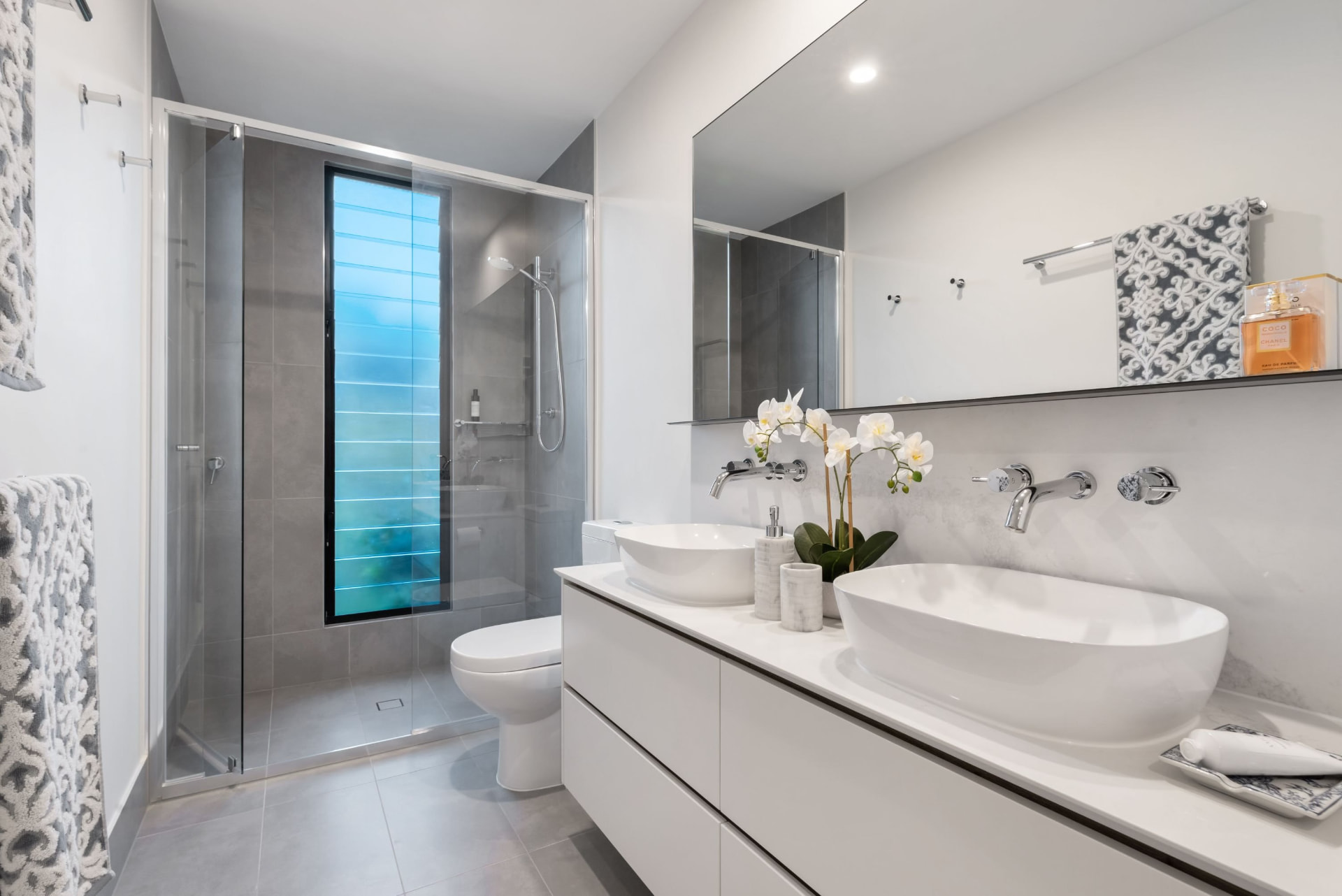 Grey tile bathroom with double vessel sinks and glass shower